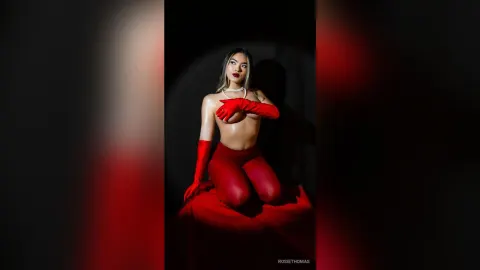 RosieThomas — Glamorous woman in red gloves and matching outfit posing against a dark studio background with dramatic lighting.