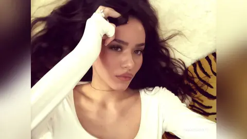Young woman with long dark hair wearing a white long-sleeve top relaxing in a cozy indoor setting.