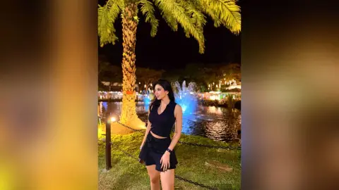 Woman in a black sleeveless top and shorts standing by a lit fountain at a tropical night resort.