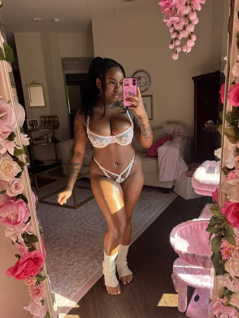 MsCookieSwirl smiles while posing in a black choker, showing her dark braided hair and bare shoulders.