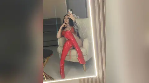 Confident woman in red lingerie and thigh-high patent leather boots posing in a mirror selfie.