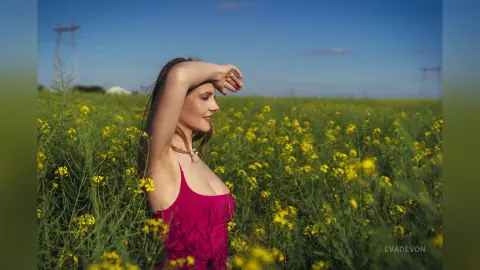 Young woman in a red tank top relaxing in a sunny yellow wildflower field under a clear blue sky.