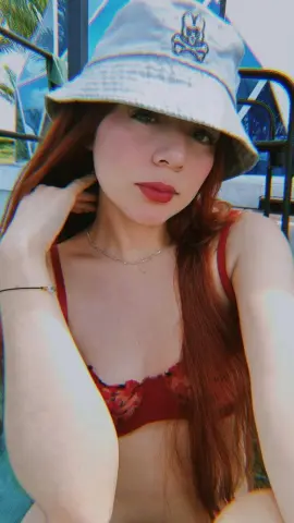 Redheaded woman in a red floral bikini and white bucket hat relaxing outdoors in sunny summer weather.