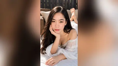 Relaxed young woman in white lace loungewear resting on a sunlit outdoor patio bed.