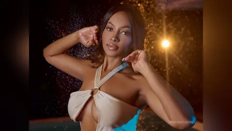 NohomiCambel poses with her hands near her face, wearing a tan halter-style top with a ring detail.