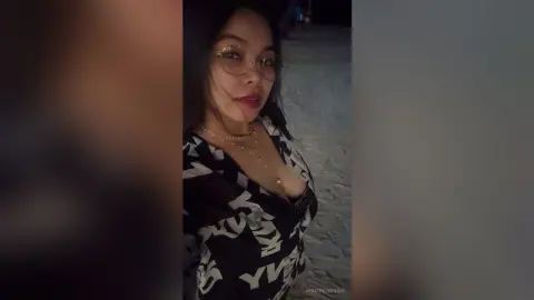 Smiling woman in glasses and a black patterned blouse posing outdoors at night.