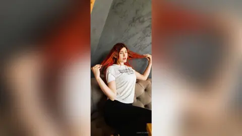 Redheaded woman in a white graphic t-shirt posing in a modern minimalist room with a relaxed mood.