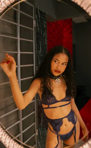 Young woman in dark lace lingerie posing confidently in front of a mirror in a moody, modern room.