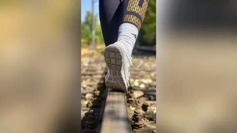 JaneHope — JaneHope walks along a railroad track wearing black leggings and grey sneakers.