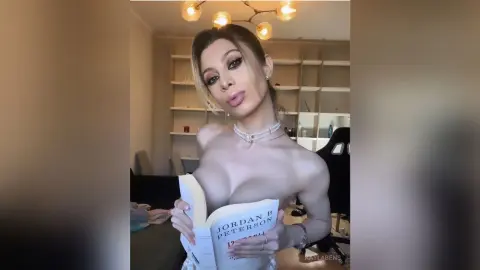 Blonde woman in a white lace outfit reading a Jordan B. Peterson book in a bright modern living room.