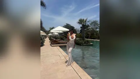 Stylish woman in a white jumpsuit standing by a luxury resort swimming pool on a sunny day.
