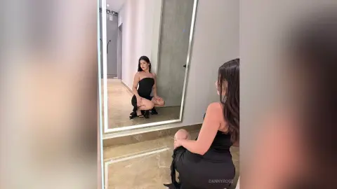 Elegant woman in a black strapless dress posing in a modern minimalist room with a large mirror.