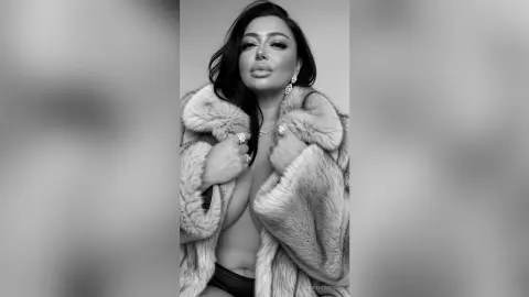 Glamorous woman in a luxury faux fur coat and diamond jewelry posing for a sophisticated black and white portrait.