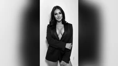Elegant woman in a black blazer suit posing confidently against a minimalist white background in black and white.