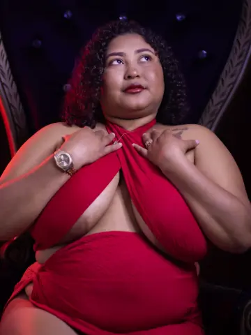 Curvy woman in a glamorous red halter dress posing elegantly in a moody, dark studio setting.