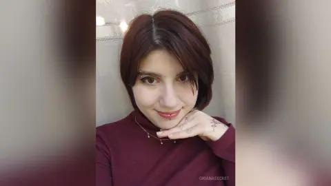 OrianaSecret — Smiling woman with short reddish hair and lip piercing wearing a burgundy turtleneck sweater indoors.