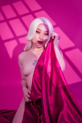 Glamorous blonde woman draped in pink satin fabric against a vibrant pink background with dramatic shadows.