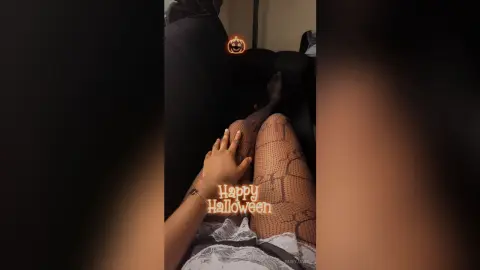 Woman in black outfit and fishnet tights relaxing on a sofa for a cozy Halloween mood.