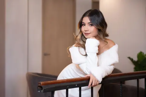 Elegant woman in a white faux fur dress posing gracefully in a modern indoor setting.