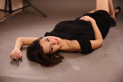 Elegant woman in a black dress lying on a studio floor with a moody, cinematic aesthetic.