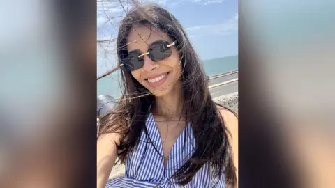 Smiling woman in sunglasses and blue striped summer top enjoying a sunny day by the ocean.