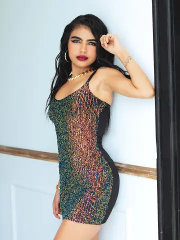 Glamorous woman in a sparkly multicolored sequin mini dress leaning against a white wall.