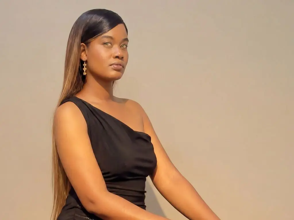 Elegant woman in a black one-shoulder dress posing against a neutral background with a sophisticated mood.