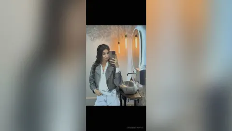 CatherineThomase — CatherineThomase takes a mirror selfie wearing a grey leather jacket and white top in a modern bathroom.