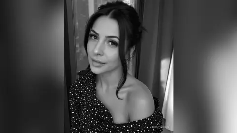 Portrait of a smiling woman in a polka dot off-the-shoulder top in a moody black and white indoor setting.