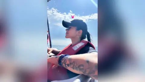 Smiling woman in a black cap and red life vest enjoying a sunny boat ride on the ocean.