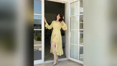 SophiaPanter stands in an open doorway wearing a long, yellow patterned dress with long sleeves and white tights.