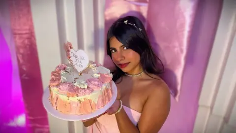 Young woman in a pink dress holding a celebratory cake for International Women's Day in a festive setting.