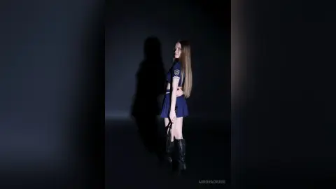 Young woman in a navy blue cosplay outfit posing against a dark studio background with dramatic shadows.