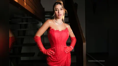 Elegant woman in a red lace evening gown and gloves posing on a dark staircase with moody lighting.