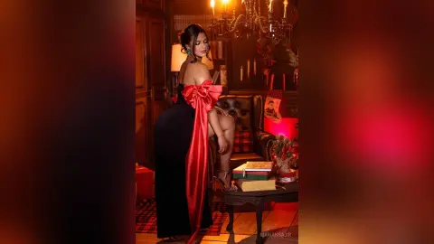 Elegant woman in a black evening gown with a red satin bow sitting in a moody, dimly lit luxury lounge.