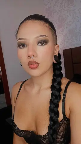 Woman with long dark braid and nose ring wearing a black lace camisole in a soft indoor setting.