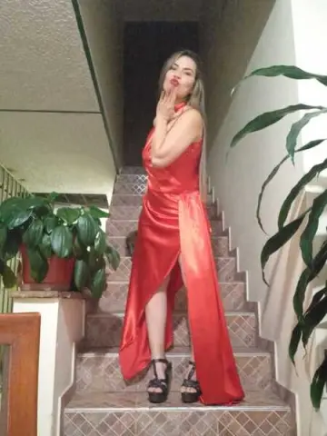 Elegant woman in a red satin evening gown posing on a staircase next to green indoor plants.