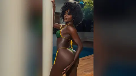 Beautiful Black woman in a green crochet bikini posing confidently by a white pillar in a sunny outdoor setting.