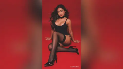 Glamorous woman in a black bodysuit and stockings posing against a vibrant red background.
