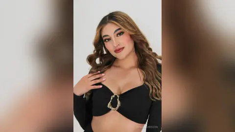 Glamorous woman in a black long-sleeve crop top with gold ring detail posing against a white studio background.