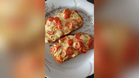 Delicious tomato and melted cheese bruschetta slices on a white patterned ceramic plate.