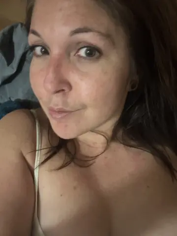 MistressBitchcoin looks at the camera with a slight pout, wearing a white tank top strap and showing her bare shoulders and chest.