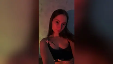 Young woman in a black crop top posing in moody, warm cinematic lighting.