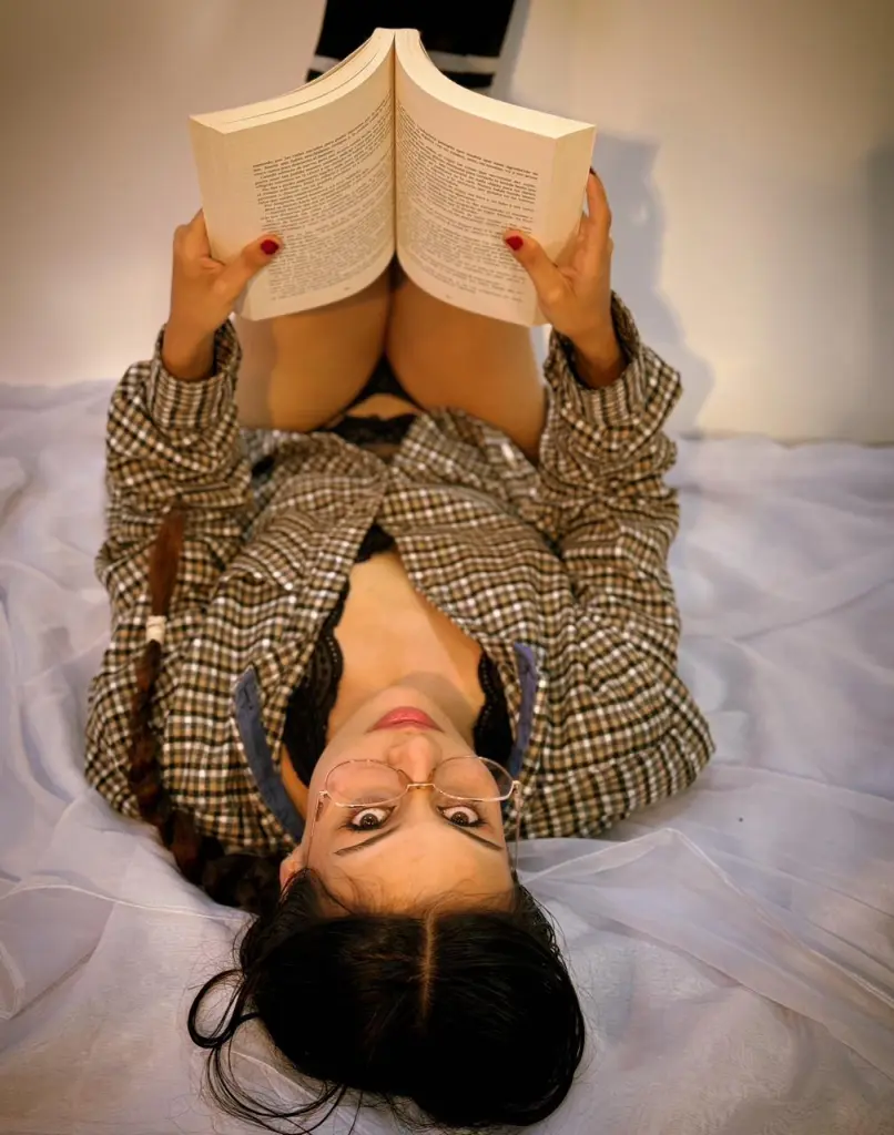 Lis_Vega looks up at the camera while wearing a white t-shirt and kneeling on a red bed.