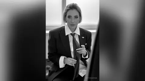 Elegant woman in a black blazer and white shirt sitting in a professional office setting, black and white portrait.