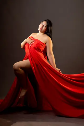 Elegant woman in a flowing red silk wrap dress posing against a dark studio background.