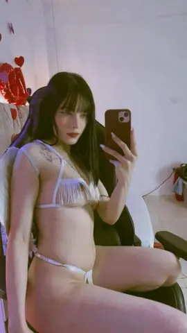 Young woman with long dark hair in white fringe bikini relaxing in a gaming chair for a casual selfie.