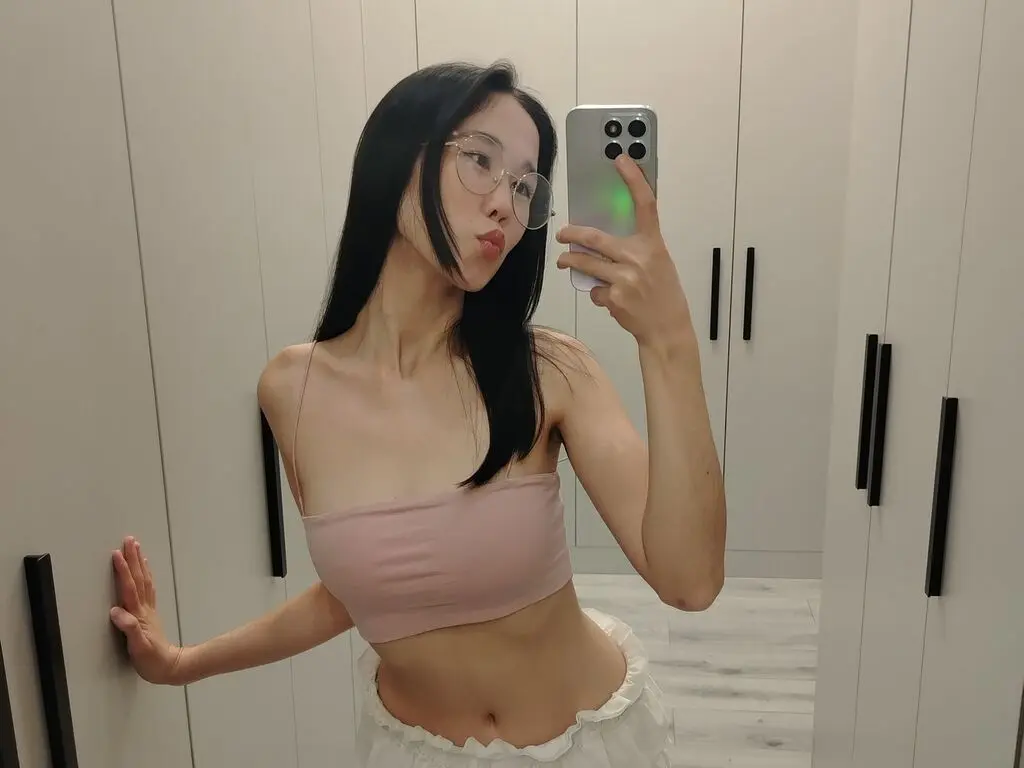 Young woman in a pink crop top taking a mirror selfie in a modern white closet setting.