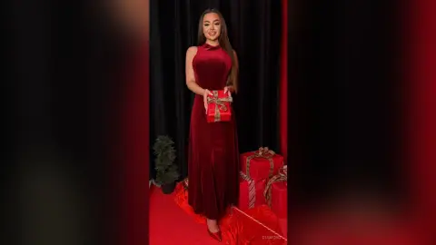 Elegant woman in a red velvet gown holding a gift box in a festive holiday setting.