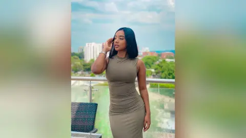 Elegant woman in a tight olive green midi dress posing on a sunny urban balcony.